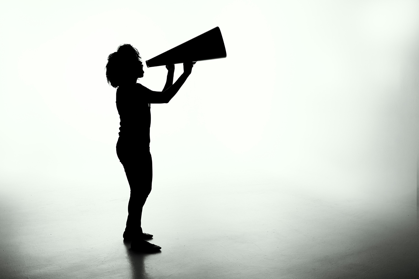 Silhouette of a woman speaking through a megaphone against a bright backdrop