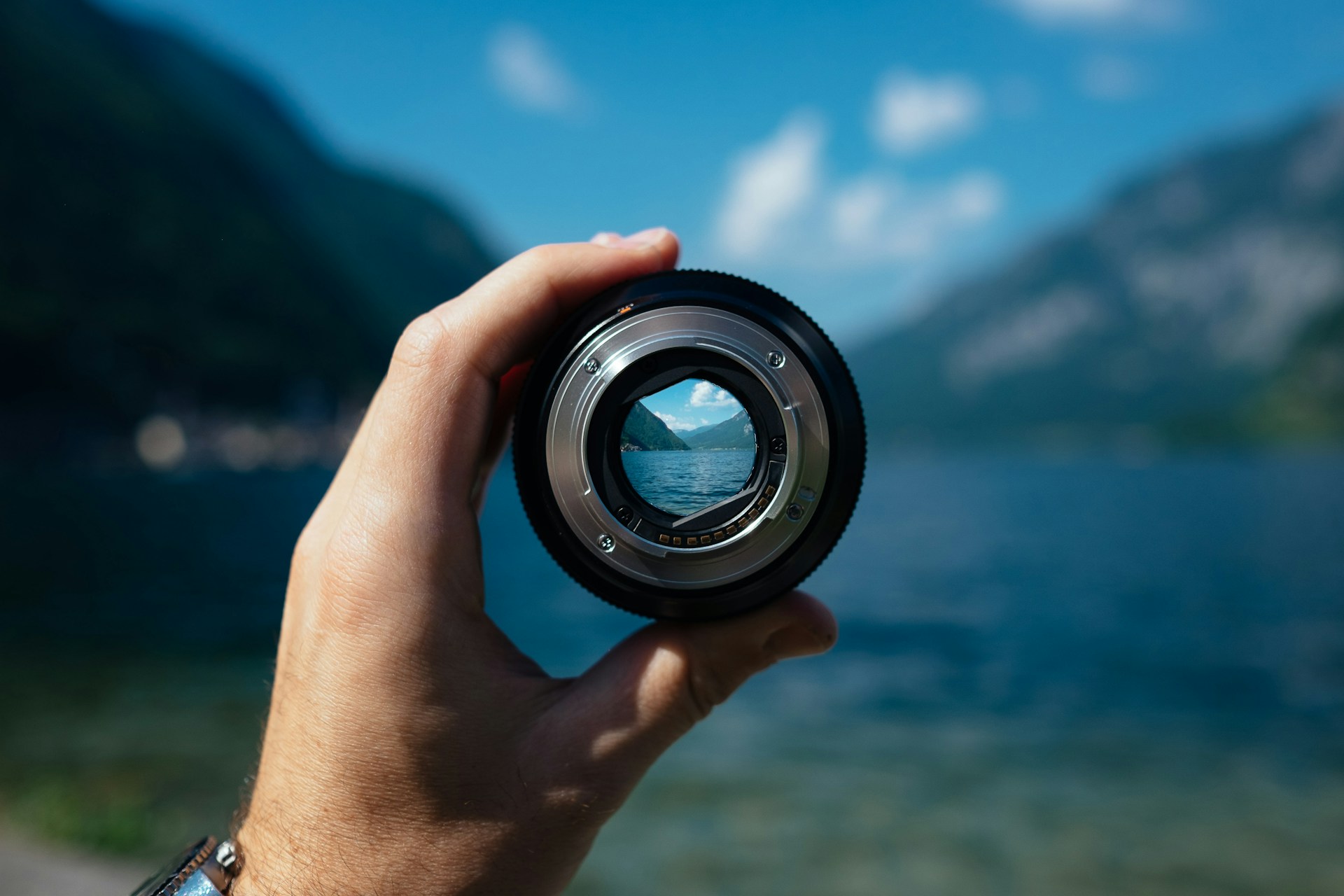 Hand holding a camera lens that brings a lake and mountains into focus